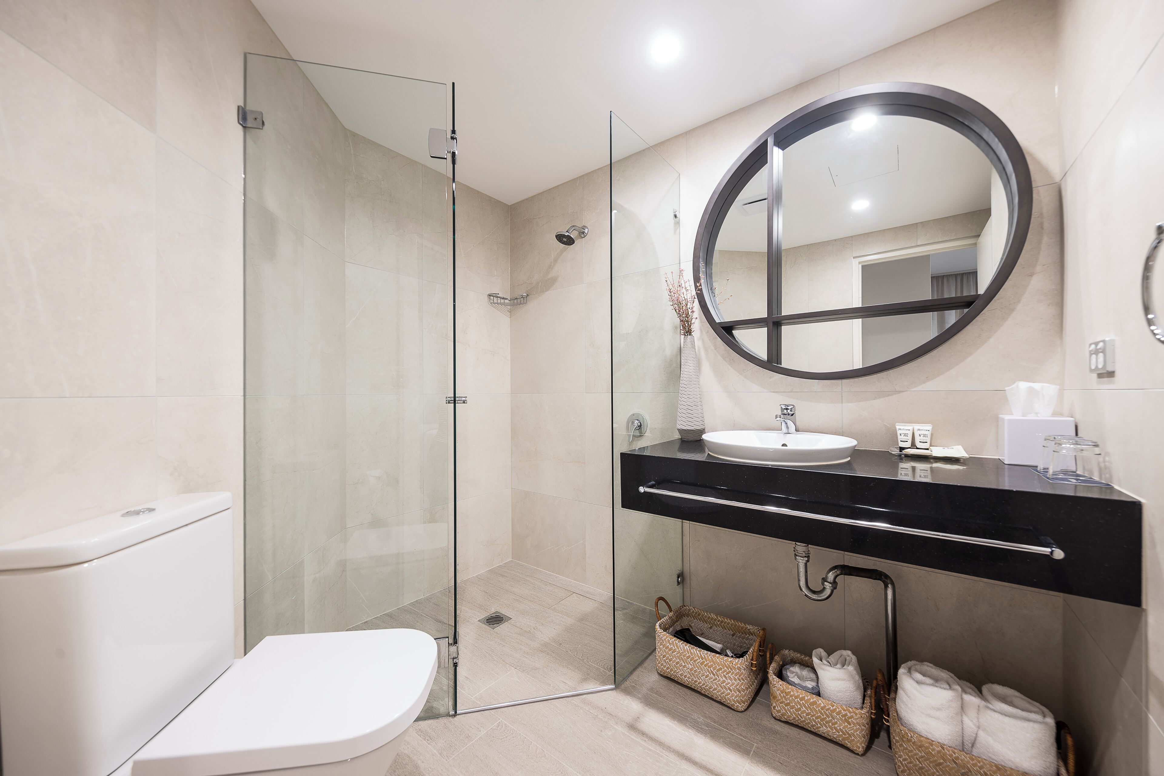 A modern bathroom with a glass-enclosed shower, a white toilet, a black sink vanity, and two wicker baskets under the counter.
