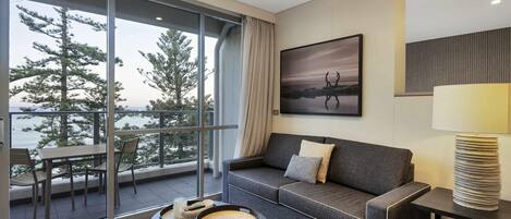 A modern hotel room with a balcony, a sofa, a coffee table, and a painting.