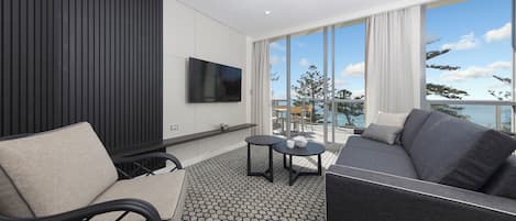 A modern living room with a sofa, armchair, and a small table. A flat-screen TV is mounted on the wall.