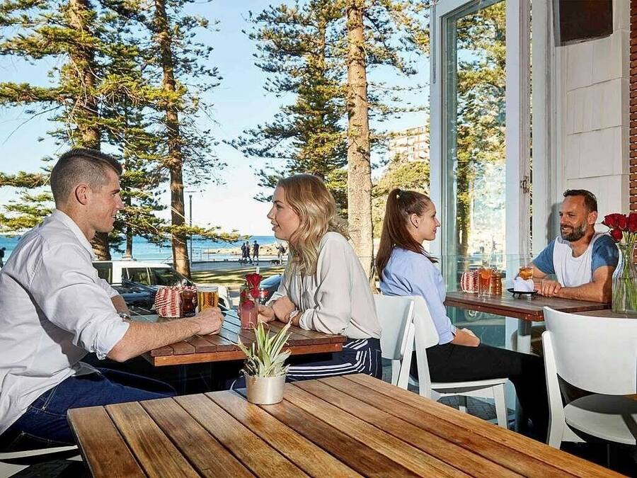 A group of people seated at wooden tables outdoors with a view of trees and a body of water.