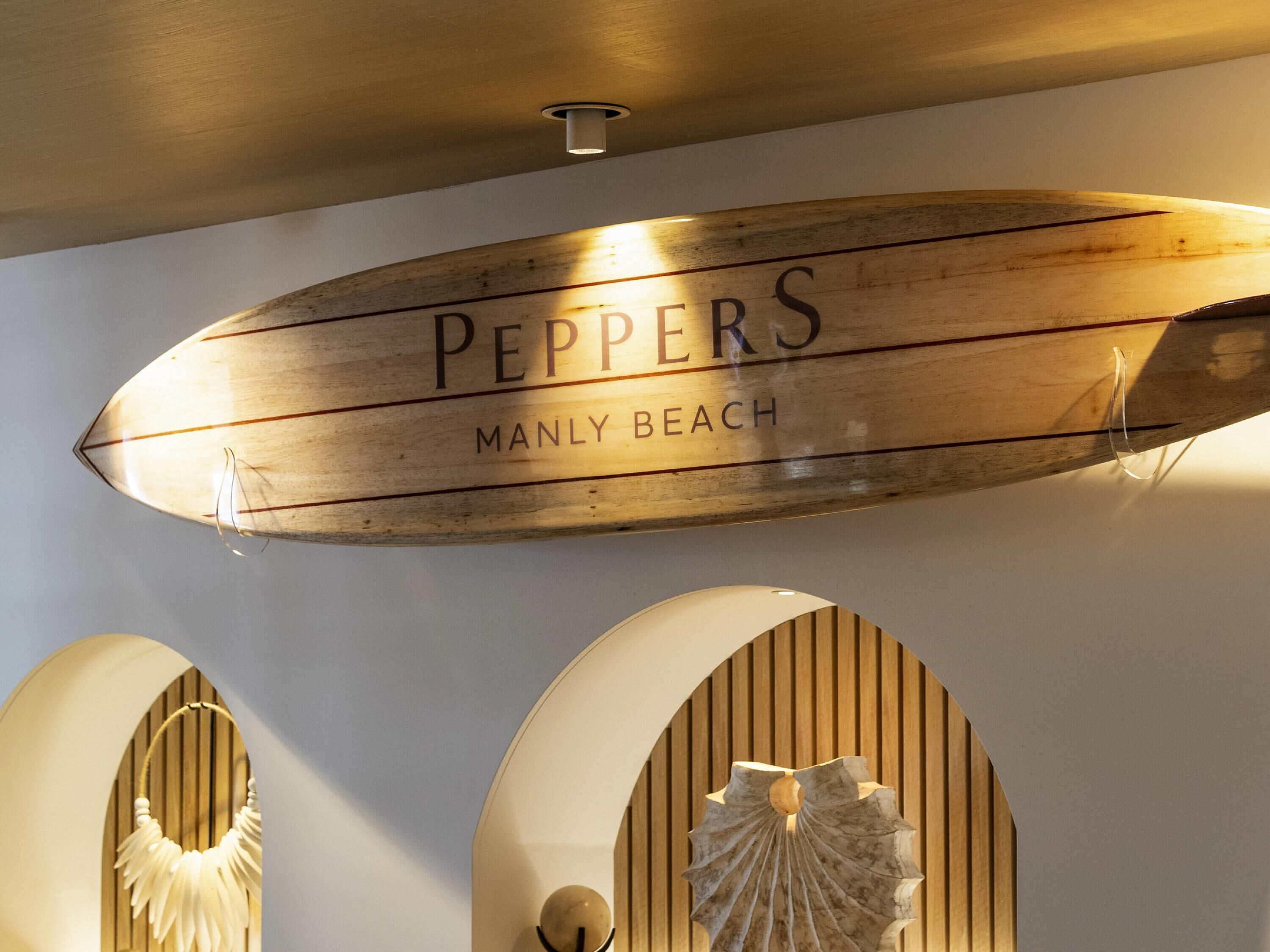 Un letrero de madera con el texto 'PEPPERS MANLY BEACH', una lámpara del techo y una escultura decorativa.