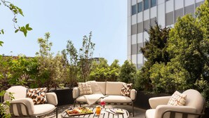 Un área de estar al aire libre con un conjunto de sofás y una mesa de centro, rodeada de vegetación y un edificio moderno al fondo.