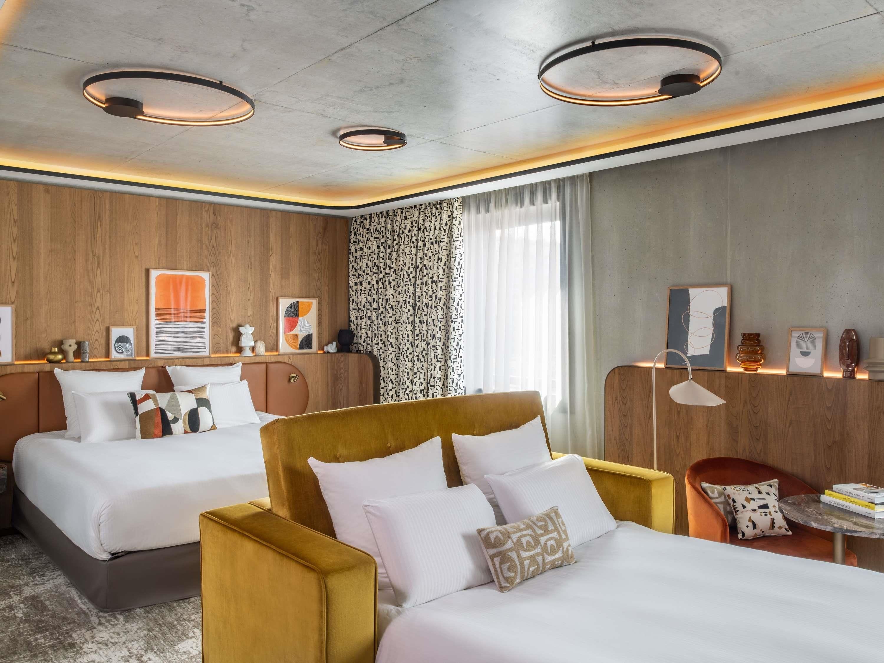 A hotel room with two beds, a sofa, a small table, and a chair.
