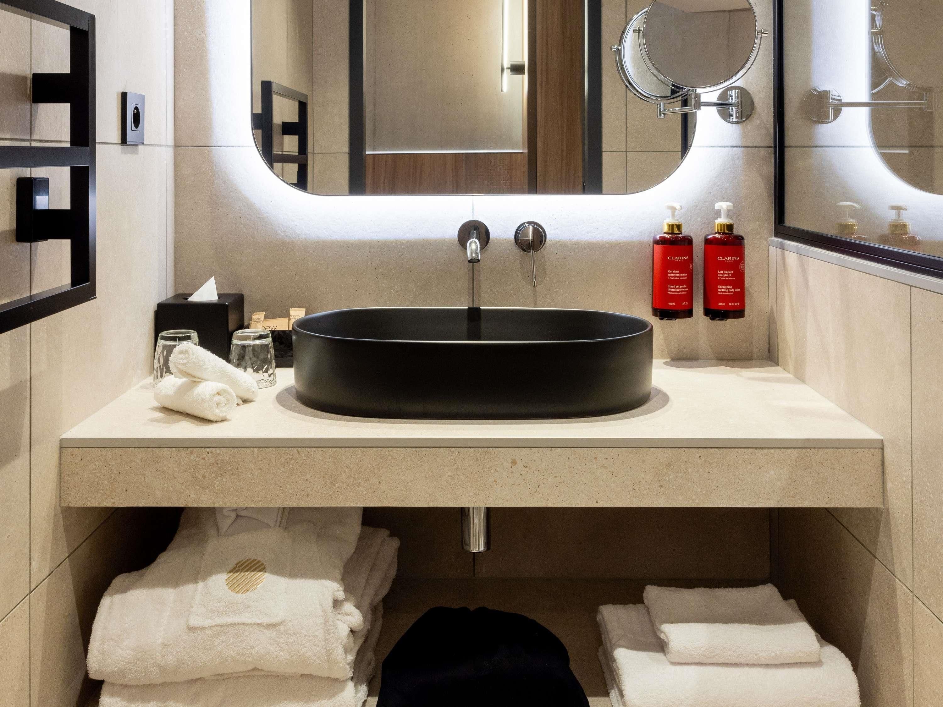 A modern bathroom with a round black sink, a mirror, and two toiletries on the counter.
