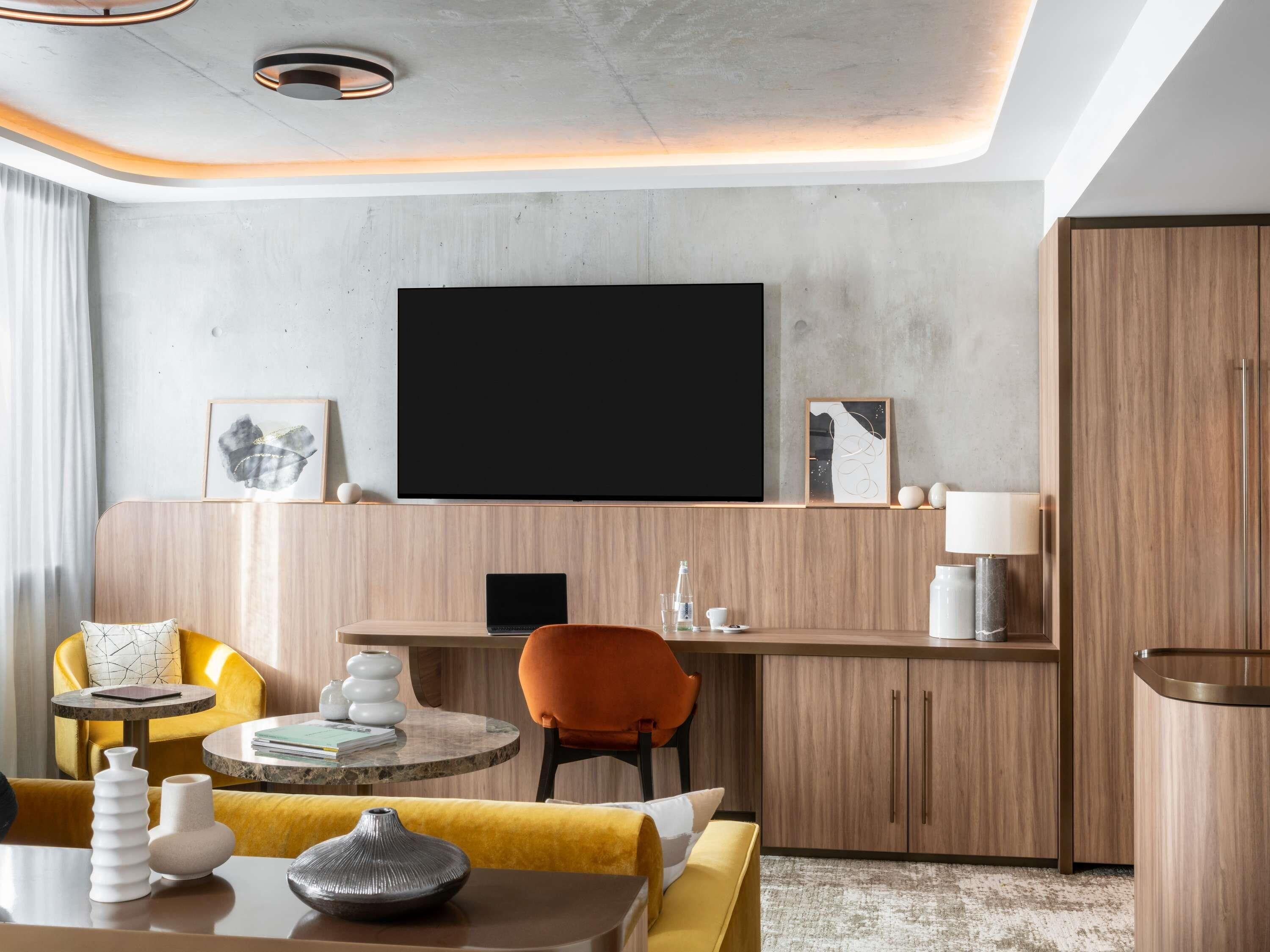 A modern living room with a flat-screen TV, wooden furniture, and a yellow sofa.