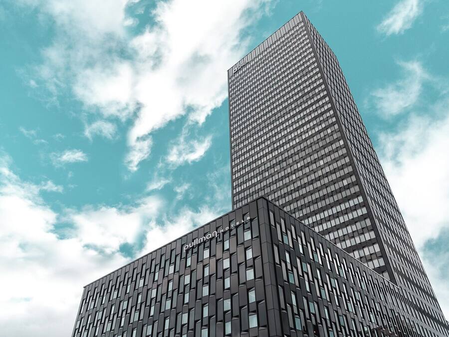 Um edifício moderno de muitos andares com fachada em grade e um edifício mais baixo com fachada padronizada em primeiro plano.