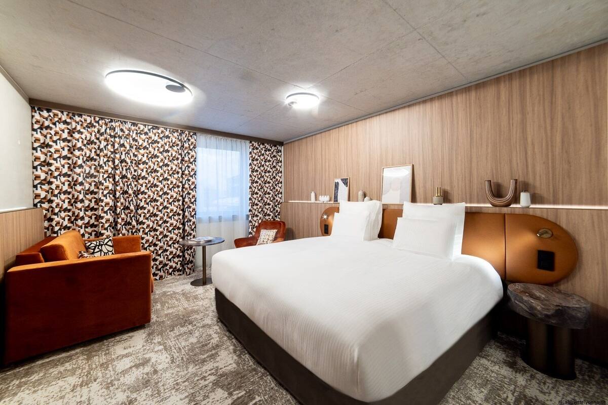 Een moderne hotelkamer met een groot bed, een rode fauteuil, een klein tafeltje en een behang met een patroon.