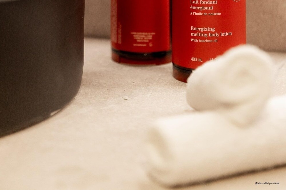 A hand dispensing lotion from a Clarins bottle into a bowl.