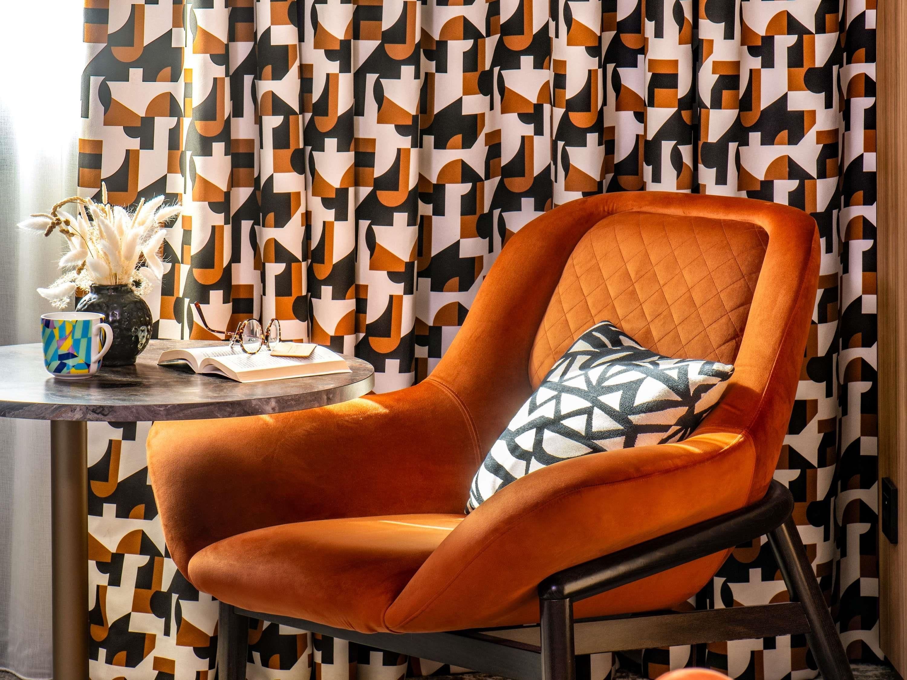 Una habitación moderna con una cortina de estampado geométrico, una mesa redonda con un jarrón, un libro y una taza.
