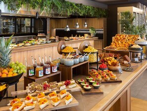 A buffet with various food items, a kitchen area, and some greenery.