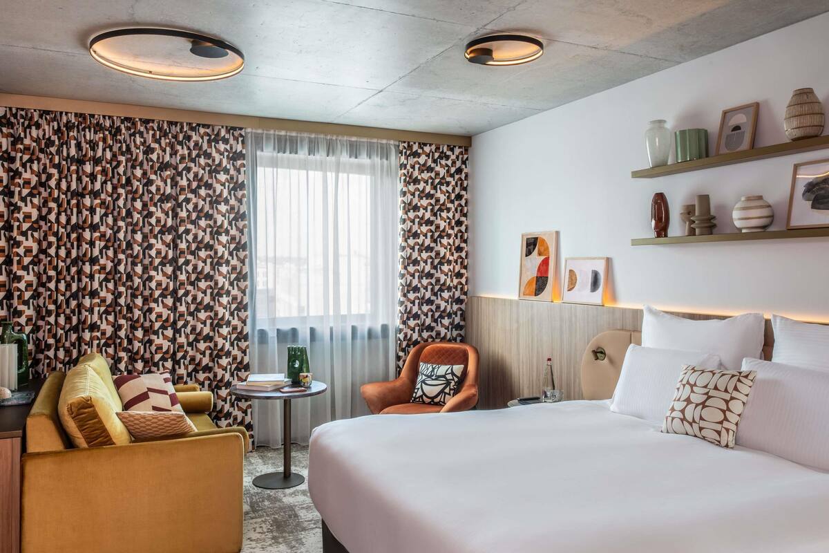 Een hotelkamer met een groot bed, een bank, een stoel, een kleine tafel en een raam met gordijnen.