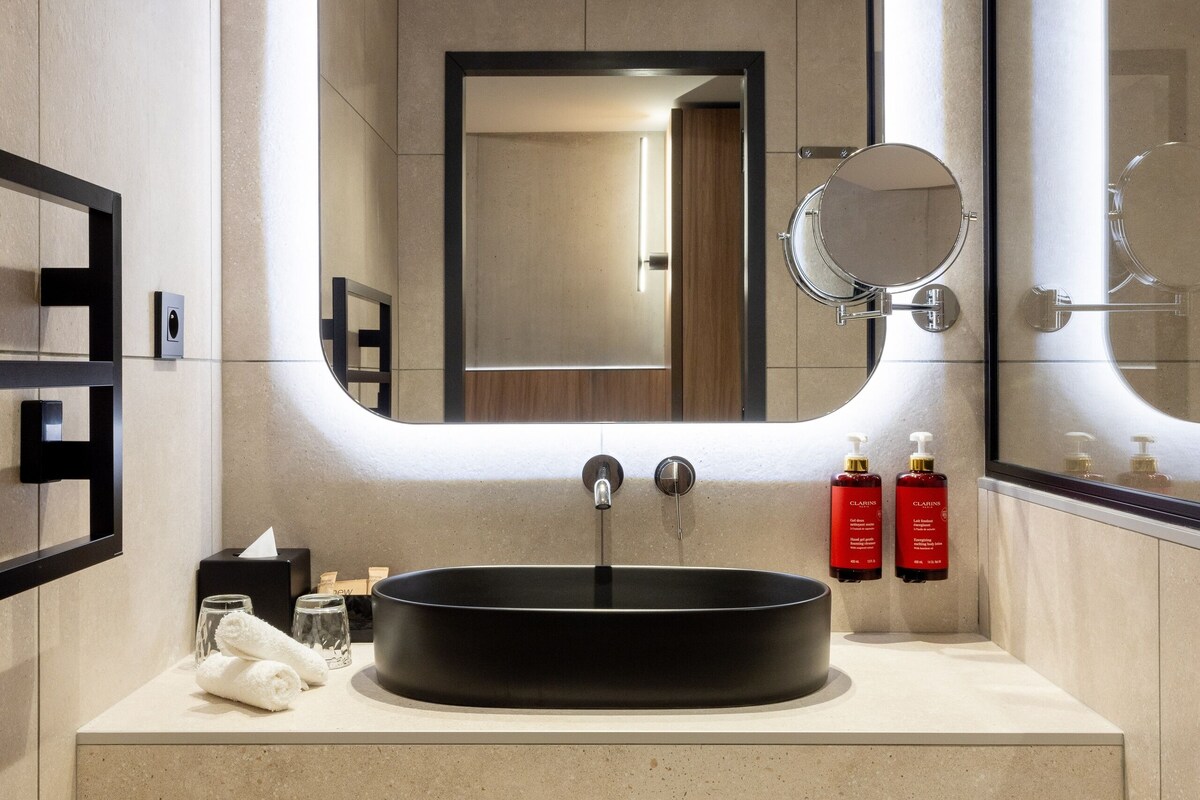 A modern bathroom with a large mirror, a round sink, and neatly folded towels.