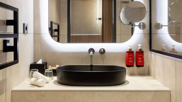 Un baño moderno con un espejo grande, un lavabo redondo y toallas ordenadas.