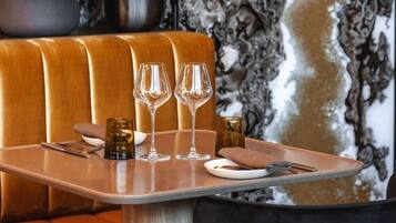 A restaurant booth with a marble wall backdrop, a potted plant, and a table set with wine glasses and a menu.