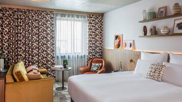 Una habitación de hotel con una cama grande, un sofá, una silla, una mesita y una ventana con cortinas.