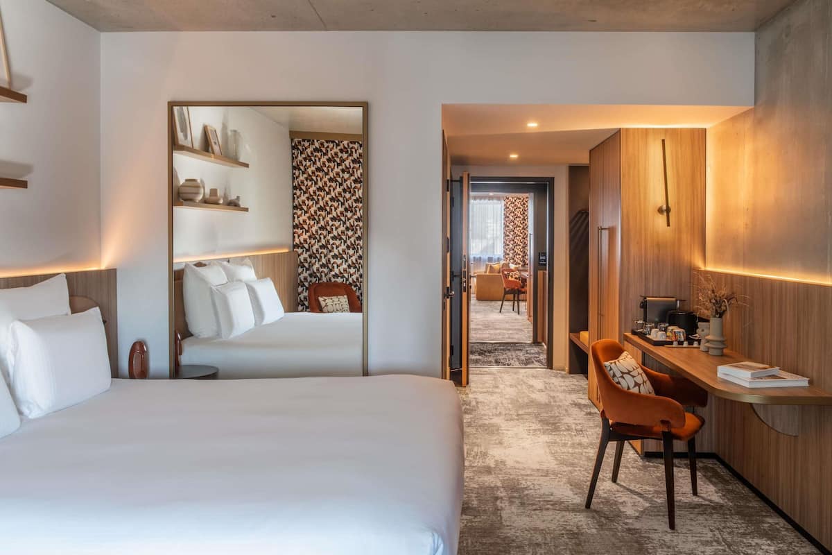 Een hotelkamer met een groot bed, een bureau met stoel, en een zithoek met een bank en fauteuils.