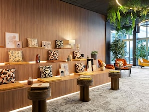 A modern lobby with wooden panel walls, a variety of patterned cushions, and a seating area with orange chairs.