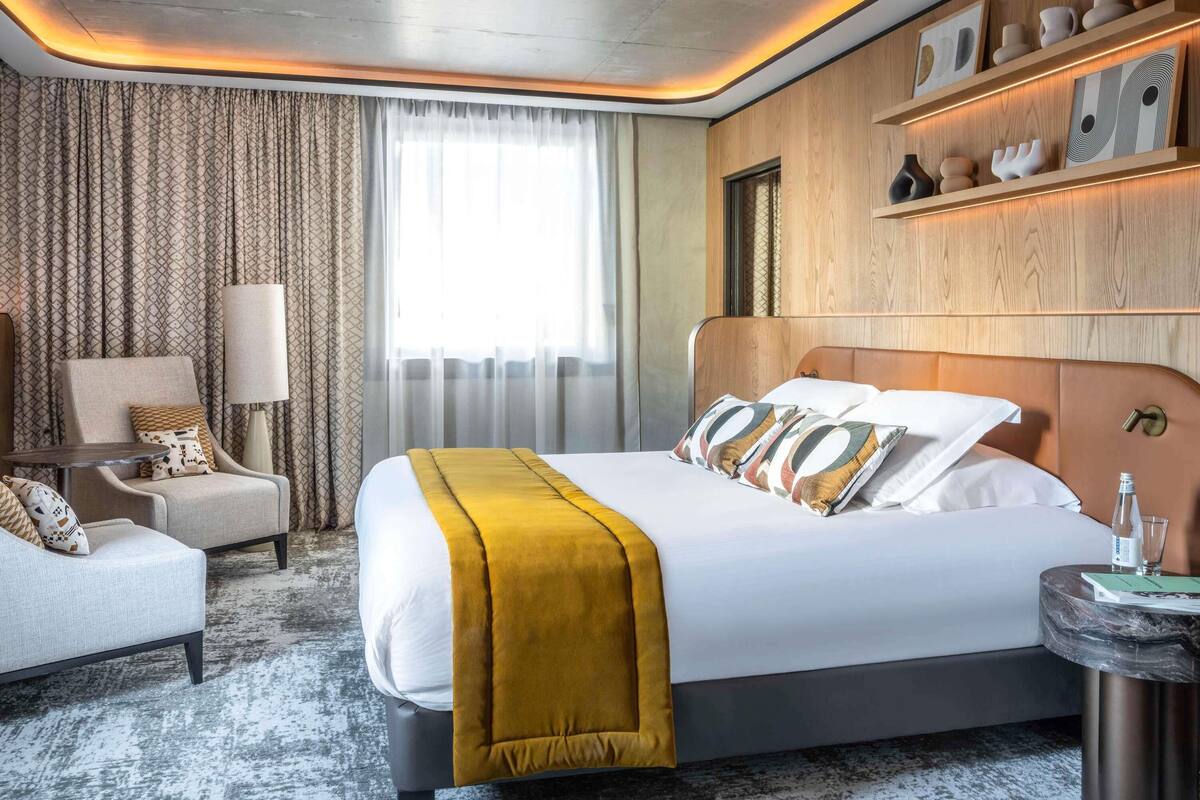 Een moderne hotelkamer met een groot bed, een zithoek met een stoel en een tafel, en een plank met decoratieve objecten.