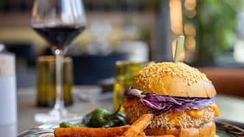 Una hamburguesa acompañada de papas fritas y una copa de vino tinto sobre una mesa.
