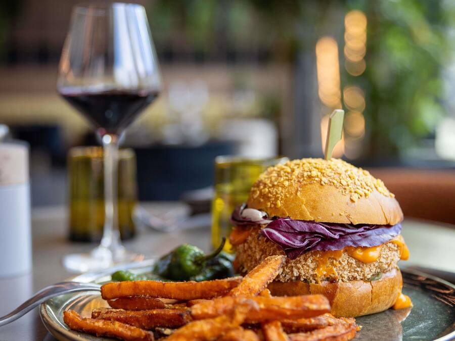 Una hamburguesa acompañada de papas fritas y una copa de vino tinto sobre una mesa.