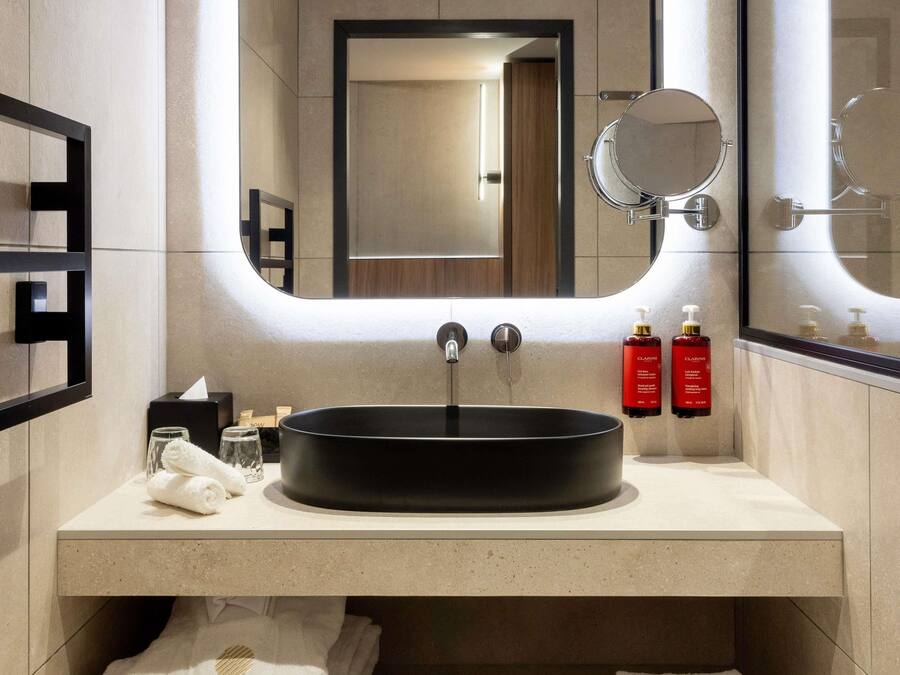 Ein modernes Badezimmer mit einem runden Waschbecken, zwei Spiegeln und Pflegeprodukten auf der Ablagefläche.