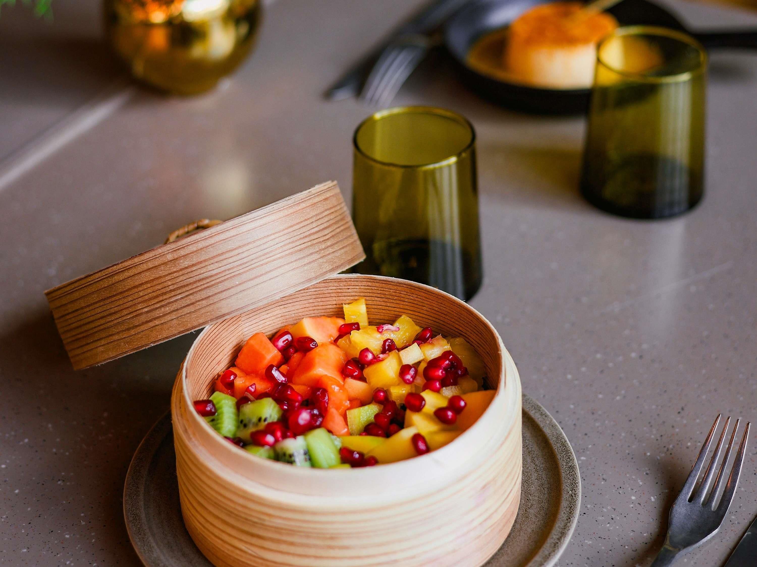 Un saladier en bois avec un couvercle, contenant une salade de fruits présentée dans une assiette.