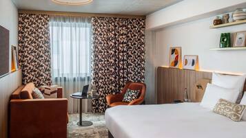 A hotel room with a bed, a sofa, a chair, a small table, and a window with curtains.