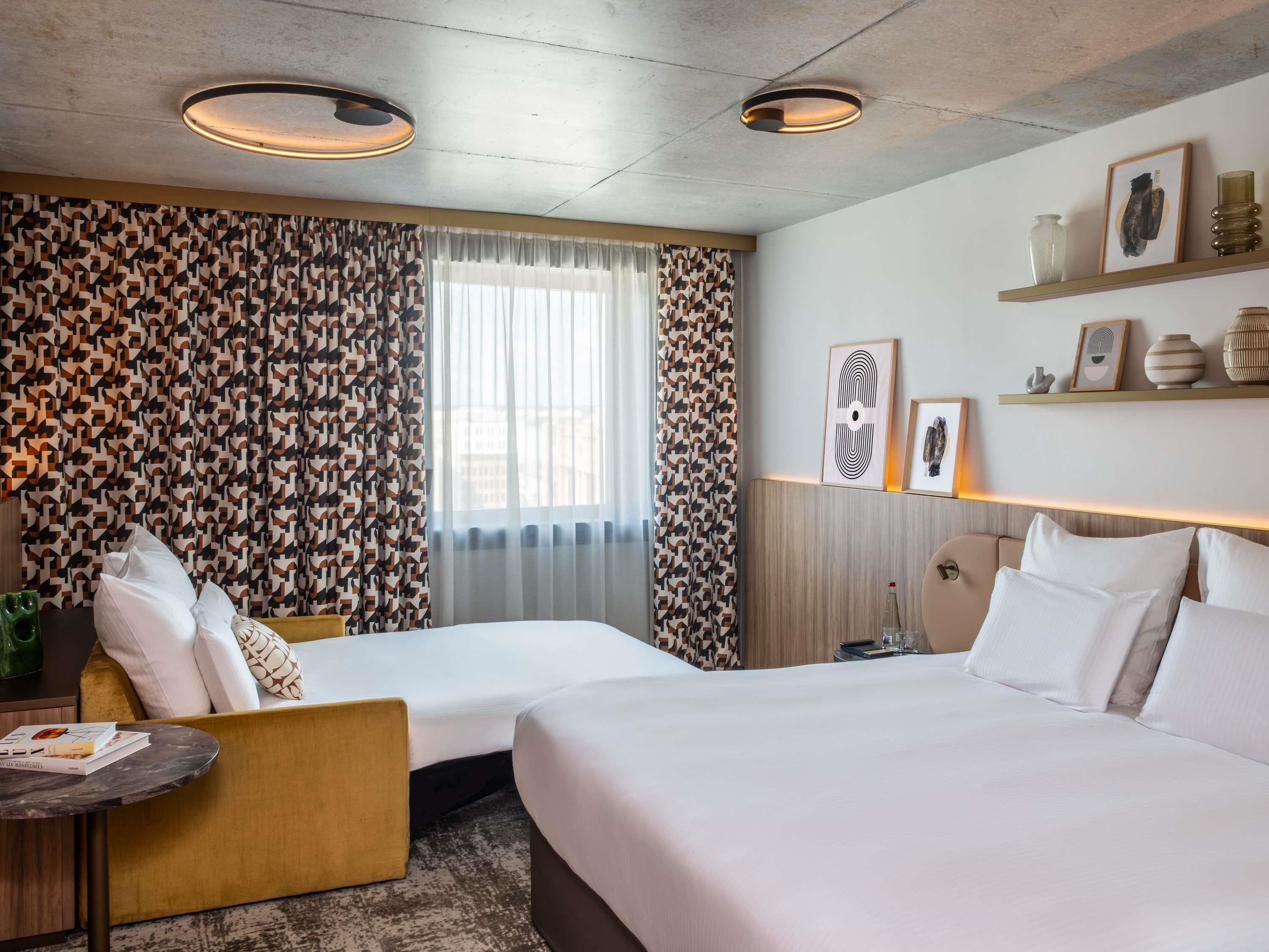 A hotel room with two beds, a sofa, a small table, and a window with curtains.