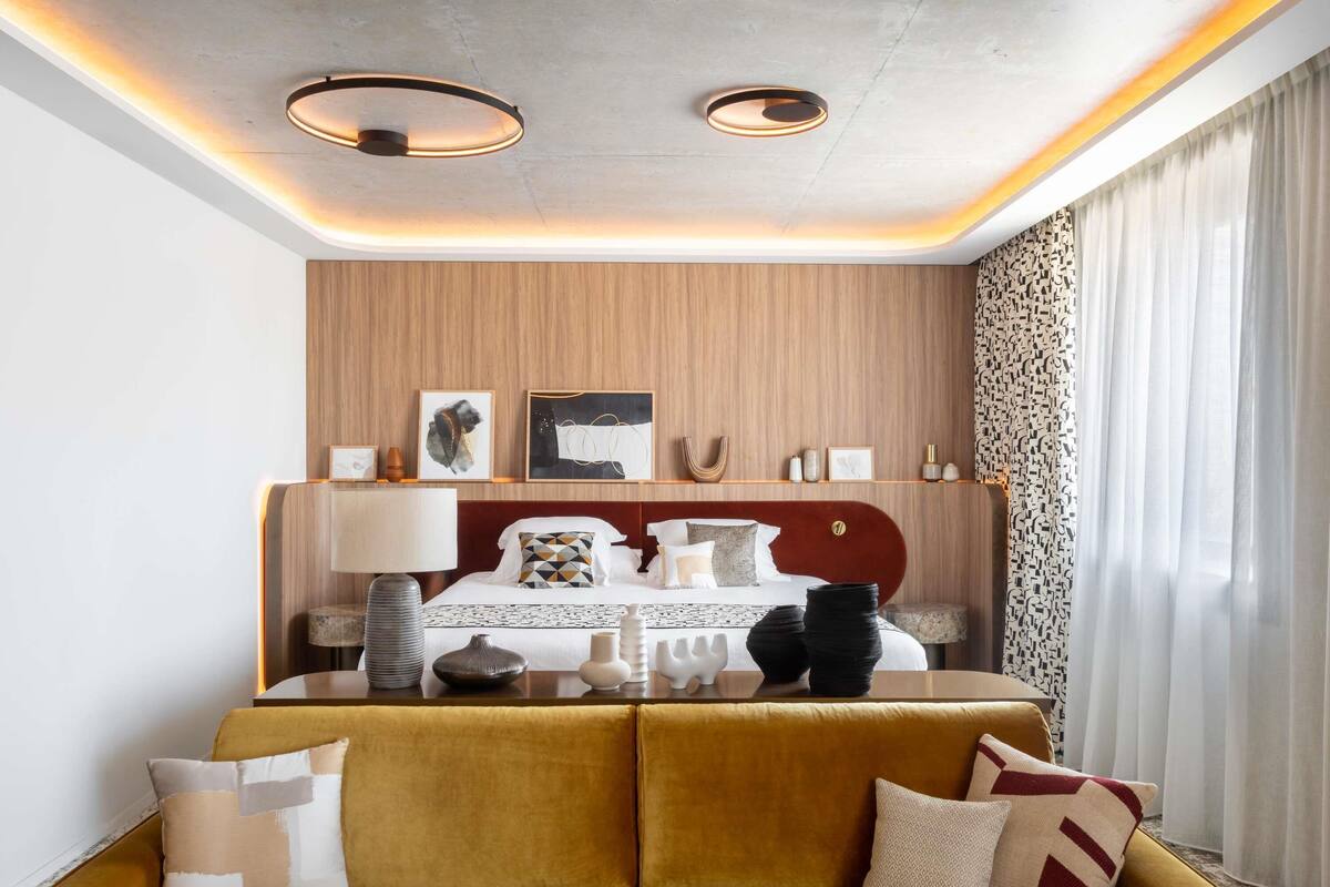 Een moderne hotelkamer met een bed, een sofa, een plafondlamp en een raam met gordijnen.