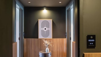 A hallway with a wooden reception desk, a wall-mounted artwork, and a digital display with a phone number.