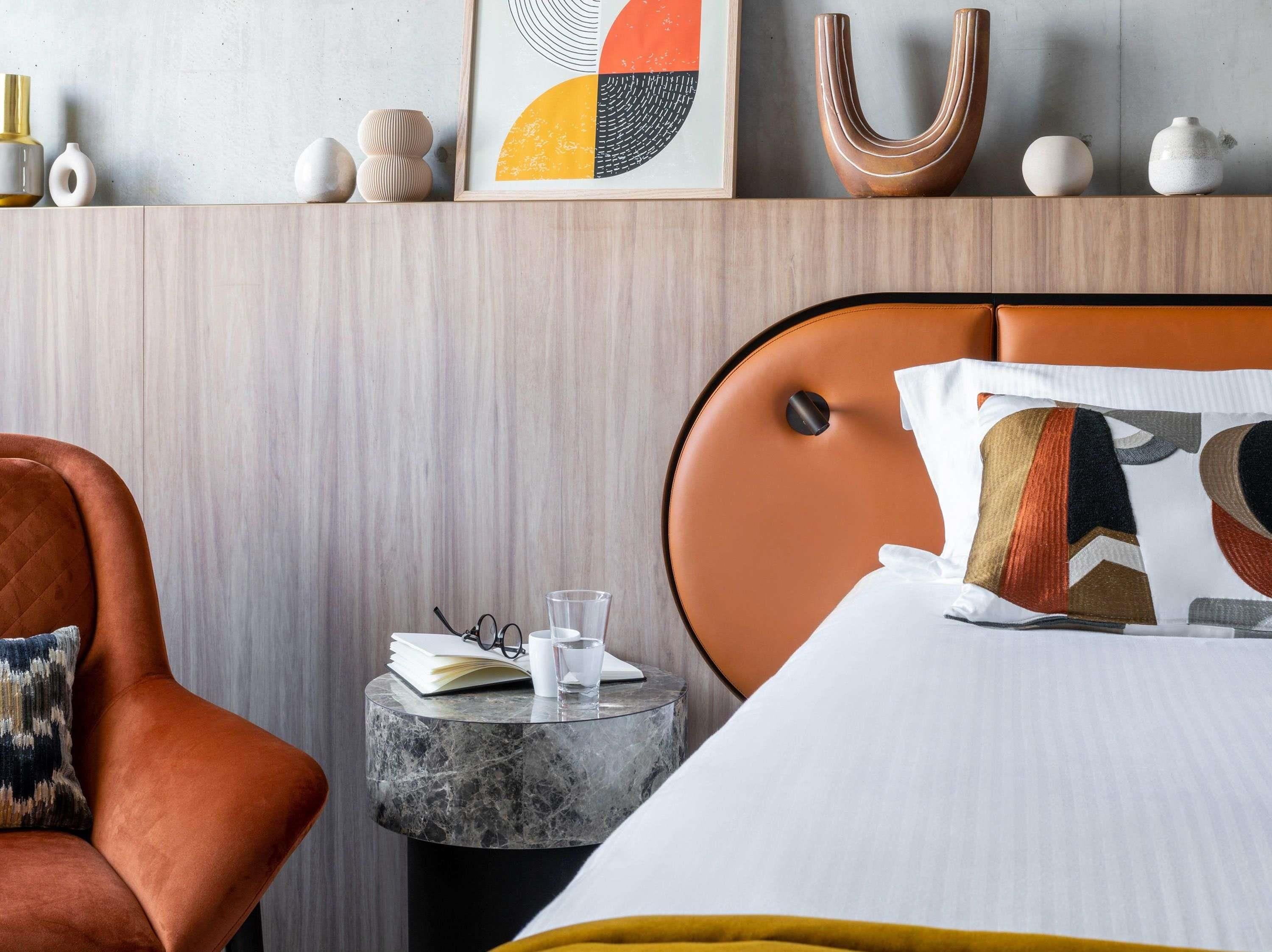 Habitación de hotel con una cama, una mesita redonda, una silla y un estante en la pared con adornos.
