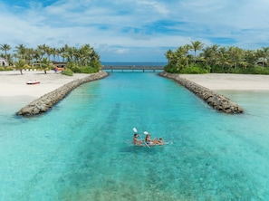 A clear turquoise waterway with a small boat in the middle, surrounded by white sandy beaches and palm trees.