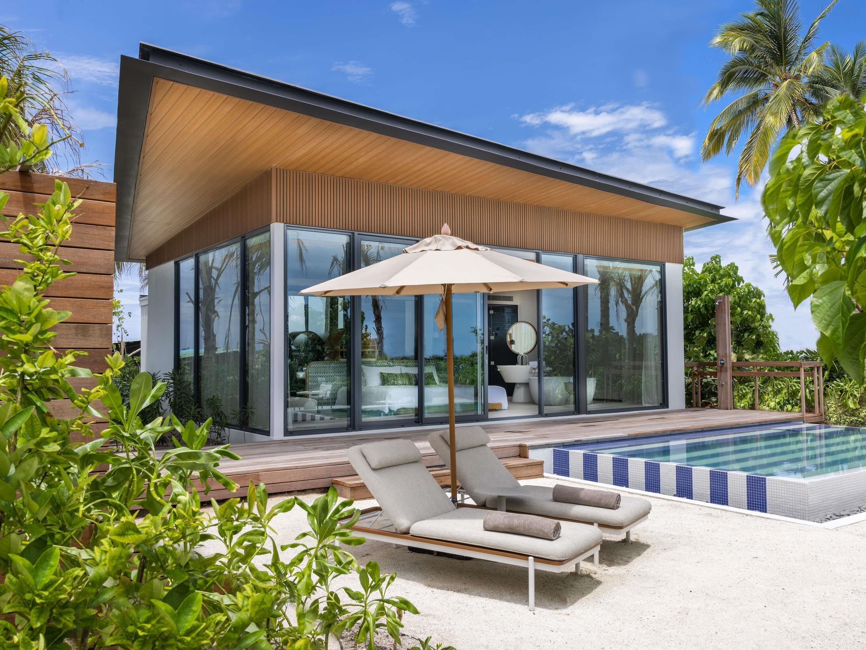 A modern house with a glass exterior, a swimming pool, and lounge chairs.