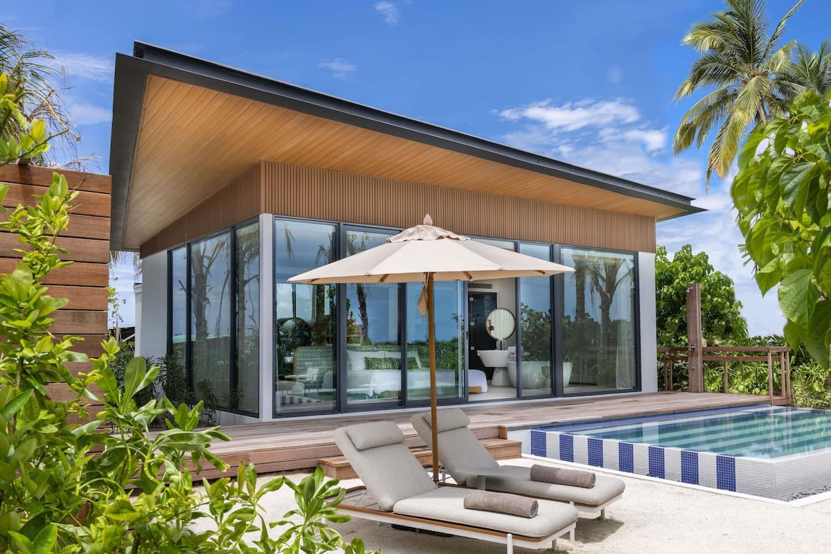 A modern house with a glass exterior, a swimming pool, and lounge chairs.