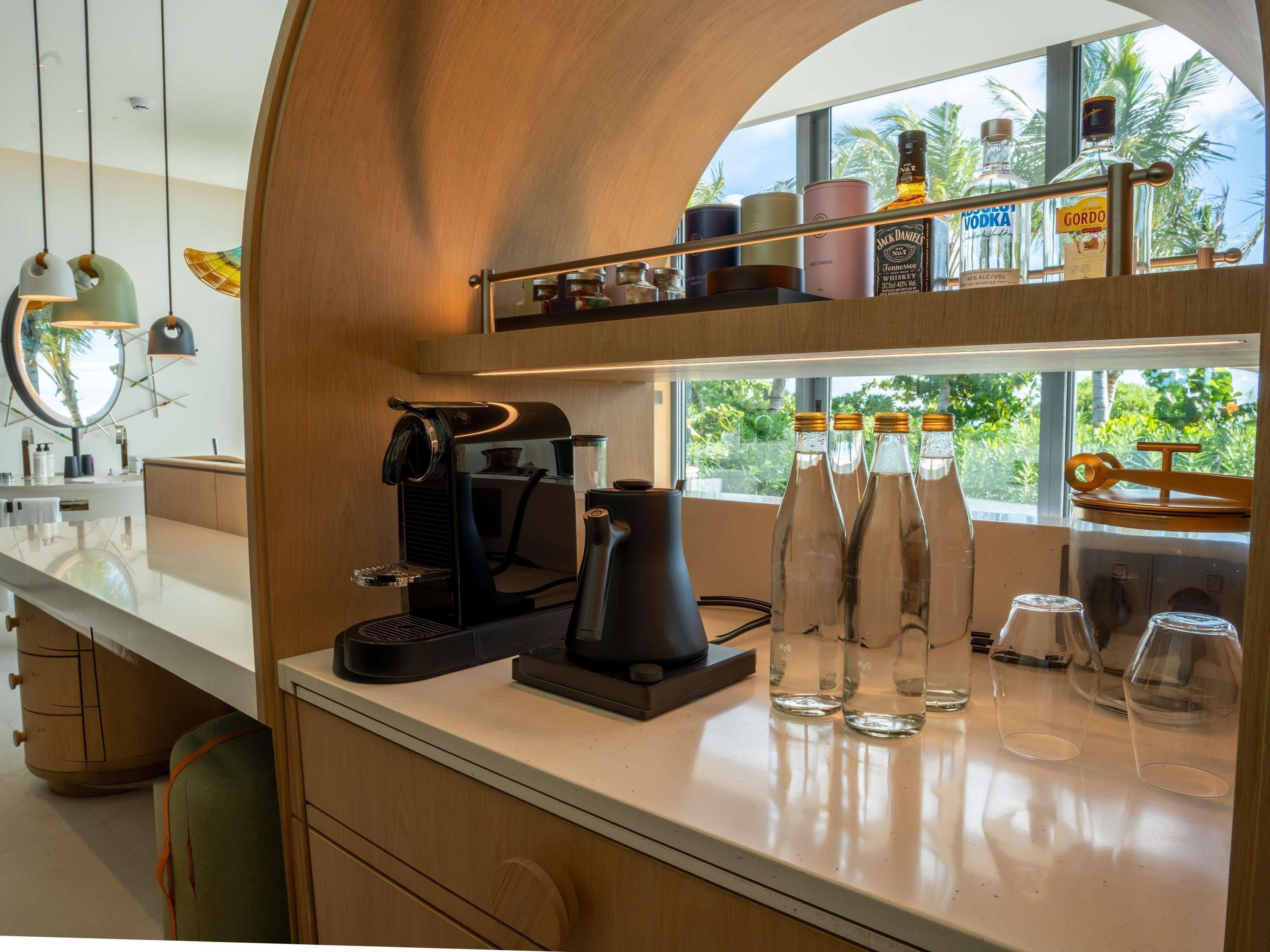 A modern kitchen with a coffee machine, water bottles, and a window with a view of palm trees.