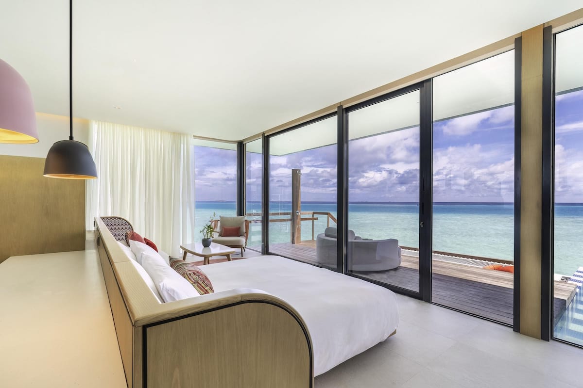 A modern hotel room with a large bed, a seating area with a view of the ocean, and a balcony with a wooden deck.