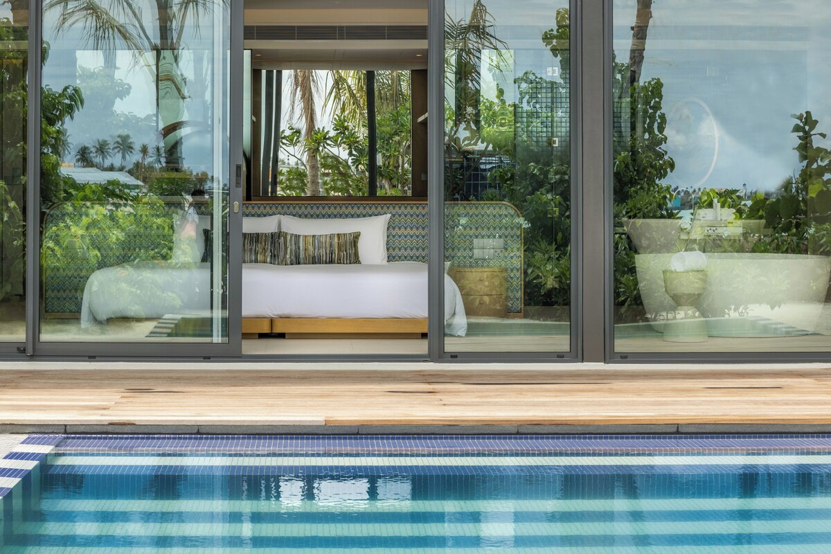 A modern hotel room with a large glass wall, a pool, and a bed with a view of the outdoors.