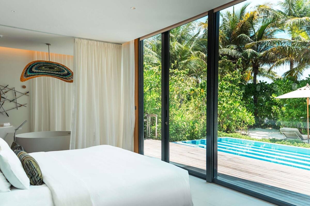 A modern hotel room with a large bed, a view of a pool, and a tropical garden.