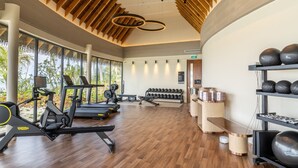 A modern gym with wooden beams, exercise equipment, and a large window overlooking greenery. - SO/ Maldives (Emboodhoo)