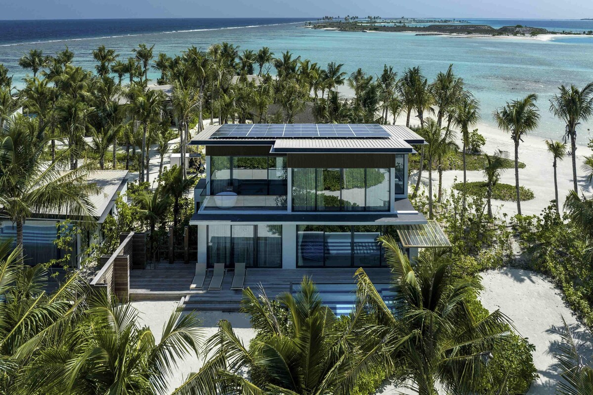 A modern beachfront property with a two-story structure, large windows, and a solar panel roof.