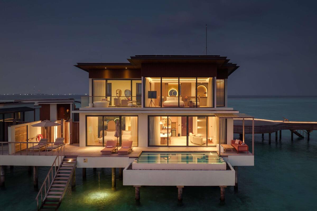 A modern multi-story resort with a pool, overwater rooms, and a pier.