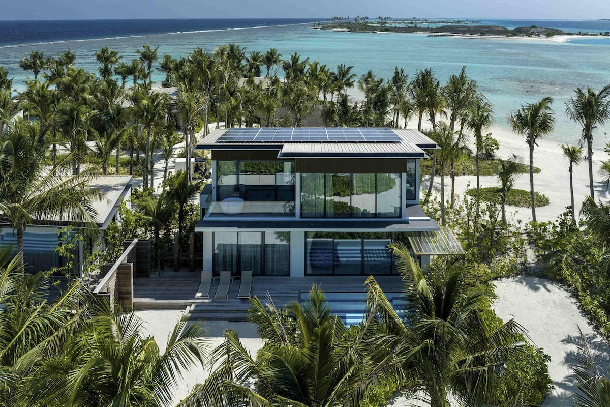 A modern beachfront property with a two-story structure, large windows, and a solar panel roof.