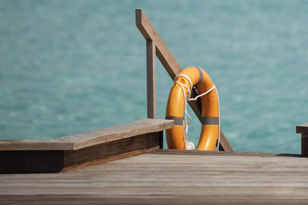 A wooden pier with a lifebuoy hanging on the railing, overlooking a calm sea.