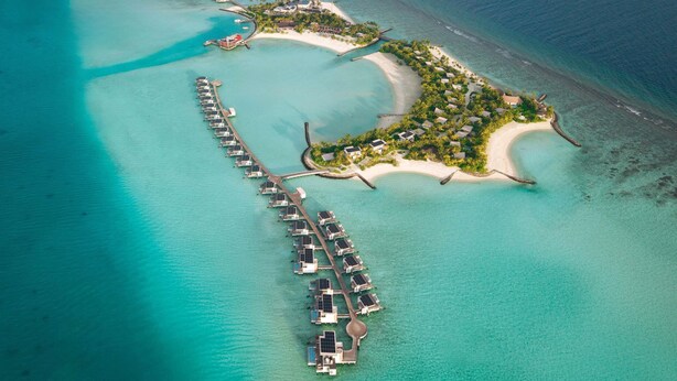 An aerial view of a resort with overwater bungalows connected by a dock, a beach area, and a small island with structures. - SO/ Maldives (Emboodhoo)