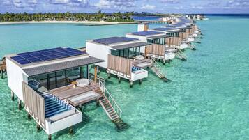 Cabañas sobre el agua con paneles solares, agua turquesa cristalina y una playa al fondo.