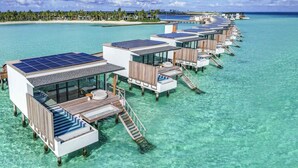 Overwater bungalows with solar panels, clear turquoise water, and a beach in the background. - SO/ Maldives (Emboodhoo)