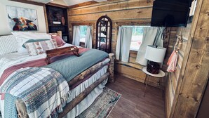 Une chambre à coucher au style rustique, avec un lit en bois, un téléviseur fixé au mur et un grand miroir.
