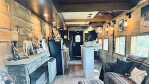 Un salon chaleureux avec une cheminée, des murs en bois et un mur d’accent en pierre. On y trouve un canapé moelleux, un fauteuil en bois et un tapis à motifs.