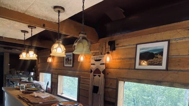 Une cuisine rustique avec un îlot central en bois, des luminaires suspendus et une grande fenêtre donnant sur la forêt.