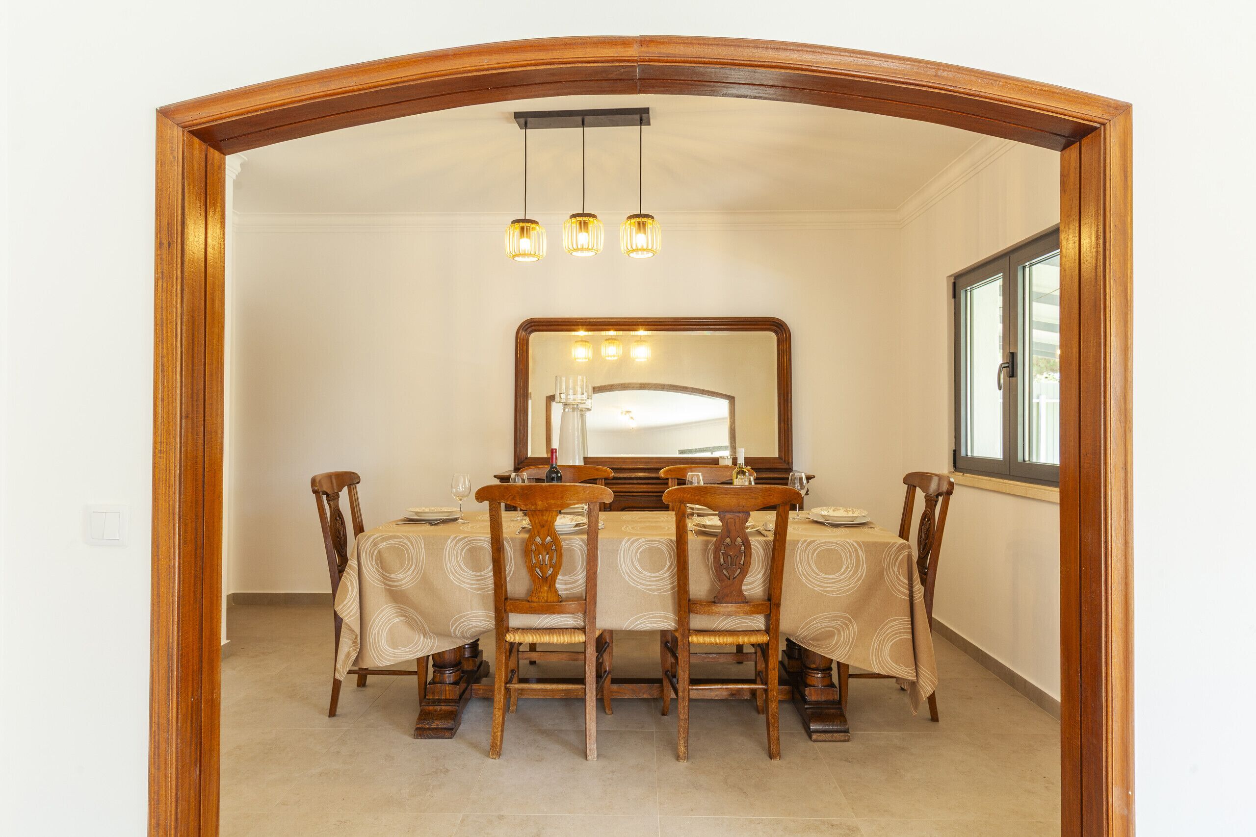 A dining room with a wooden-framed arch, a large mirror, and a chandelier.